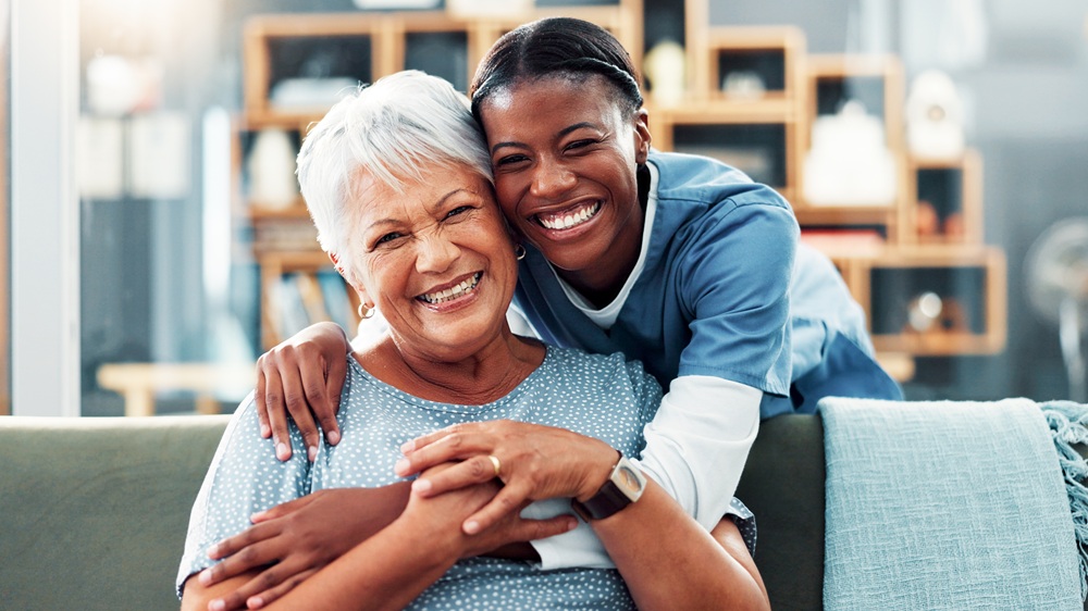 Happy senior woman and caregiver smiling together on couch, representing compassionate dental care – Loving Dentistry