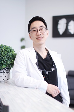 Portrait of Dr. Brian Han wearing white coat and dental loupes in contemporary clinic setting – Loving Dentistry
