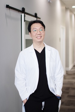 Portrait of Dr. Dongho Kim smiling in white coat standing in dental office hallway – Loving Dentistry